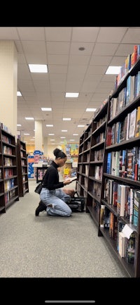 a person kneeling down in the middle of a book shelf